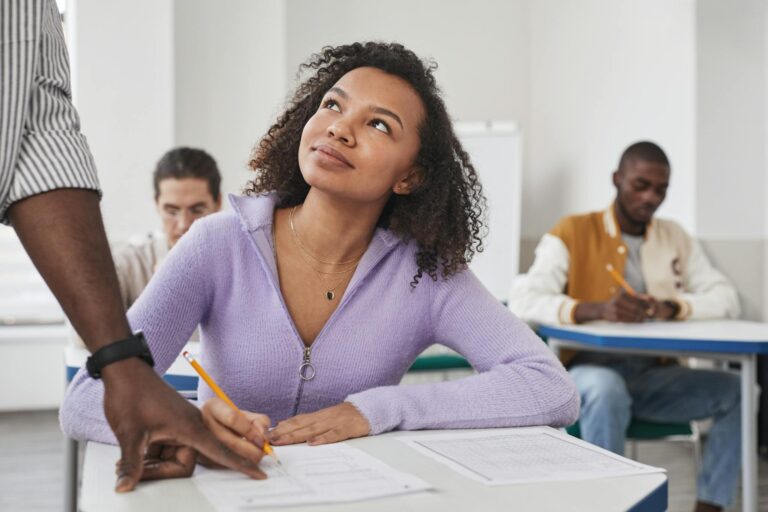 Young woman in purple sweater taking an exam in a classroom setting with peers.