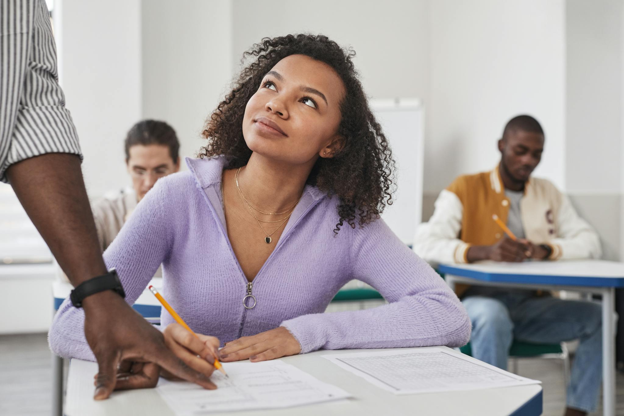 Young woman in purple sweater taking an exam in a classroom setting with peers.